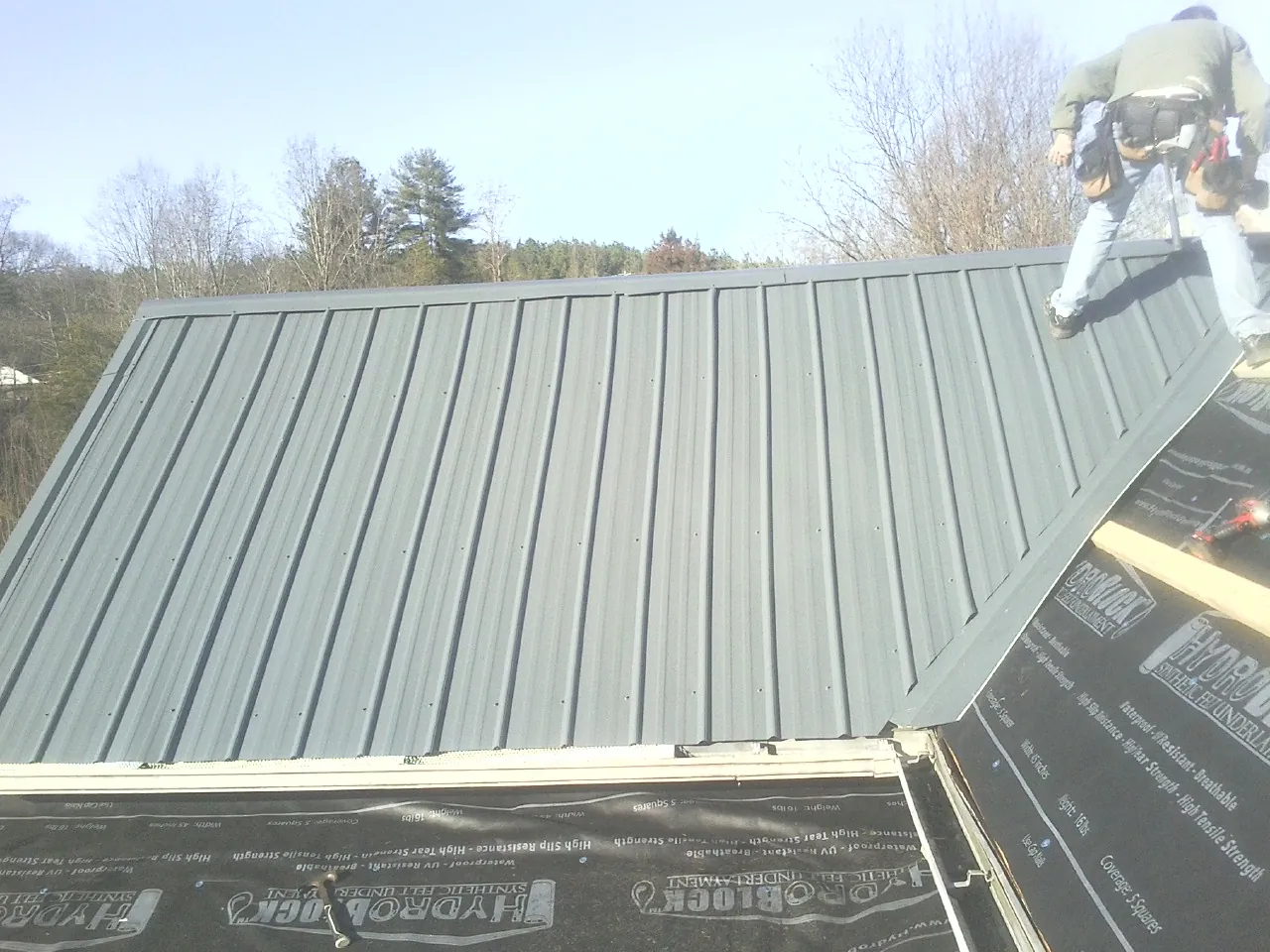 Crew installing dark green standing seam panels over synthetic underlayment in Ravenel