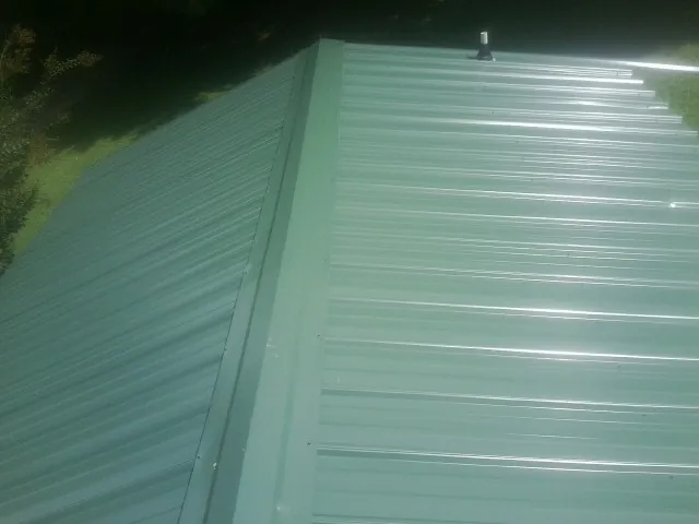 New green metal panels meeting at the ridge of a roof — Flat Roof Repair work by our crew in Ravenel