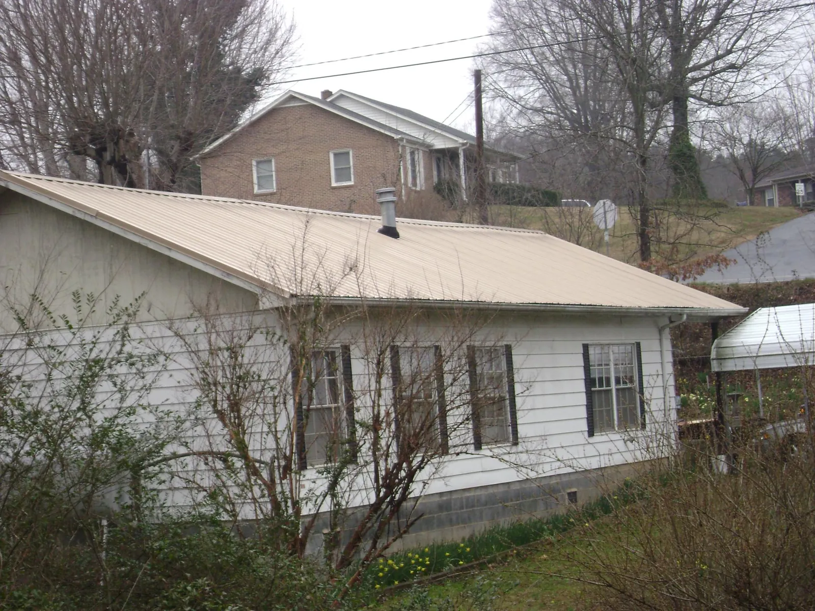 Tan metal roof on a white sided house set into a hillside — Commercial Roofing by Roofing Brothers in Ravenel